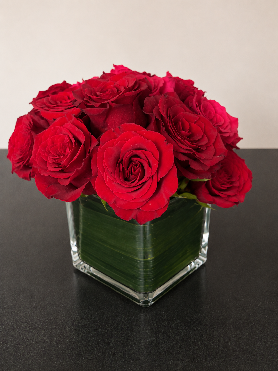 Compact arrangement of red roses in a glass cube vase